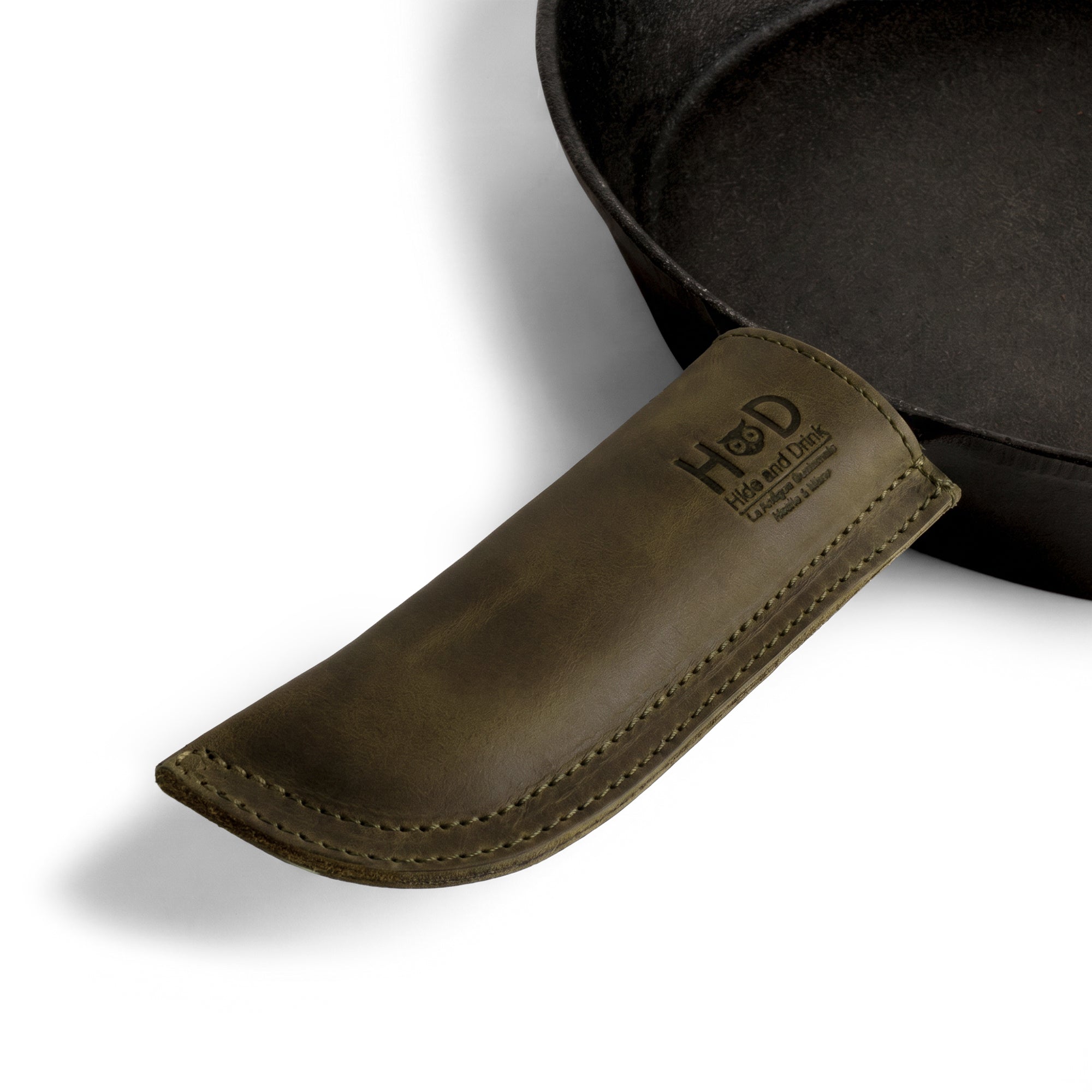 Hide & Drink Cast Iron Panhandle Cover beautifully displayed, emphasizing its unique craftsmanship. This artisan hot handle protector is made from full grain leather with double stitching for enhanced durability and comfort. Handmade in La Antigua Guatemala & Oaxaca Mexico, it's an essential kitchen accessory.