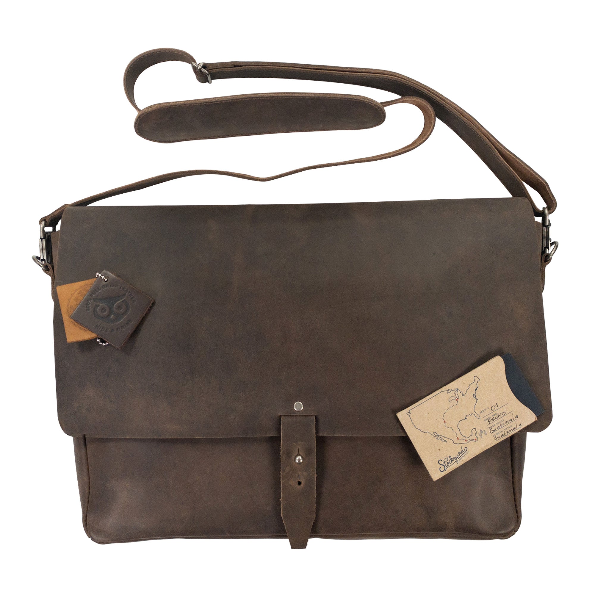 Close-up of Hide & Drink's Messenger Bag with Adjustable Strap, displaying leather tags and the quality of materials used. This travel accessory offers 13-14 inch laptop storage and features a classic portfolio design, embodying small batch production and artisan handmade craftsmanship. Handmade in La Antigua Guatemala & Oaxaca Mexico.