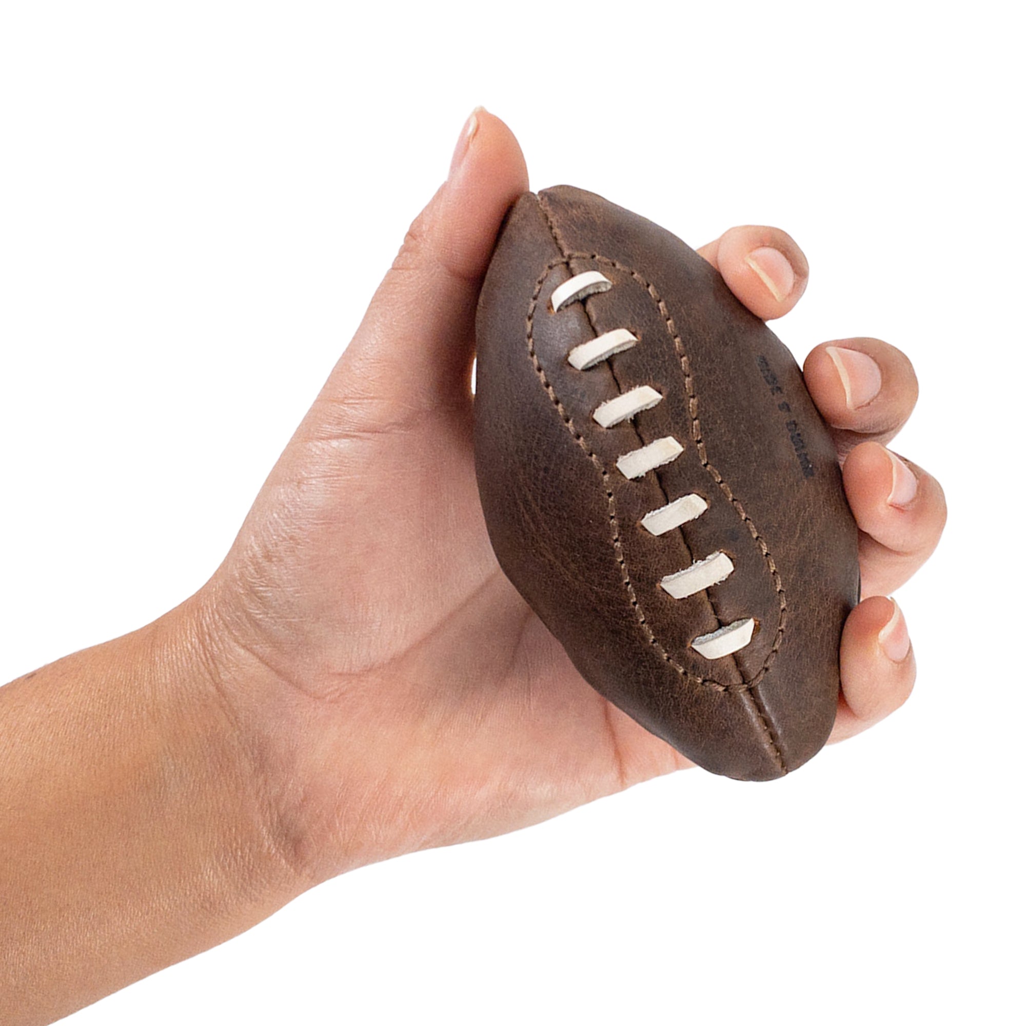 A hand gripping a Mini American Football by Hide & Drink, illustrating its perfect fit and unique shape. Made from high-quality full grain leather, this handstitched football is a memorable decorative item and an artisan keepsake, made in La Antigua Guatemala & Oaxaca Mexico.
