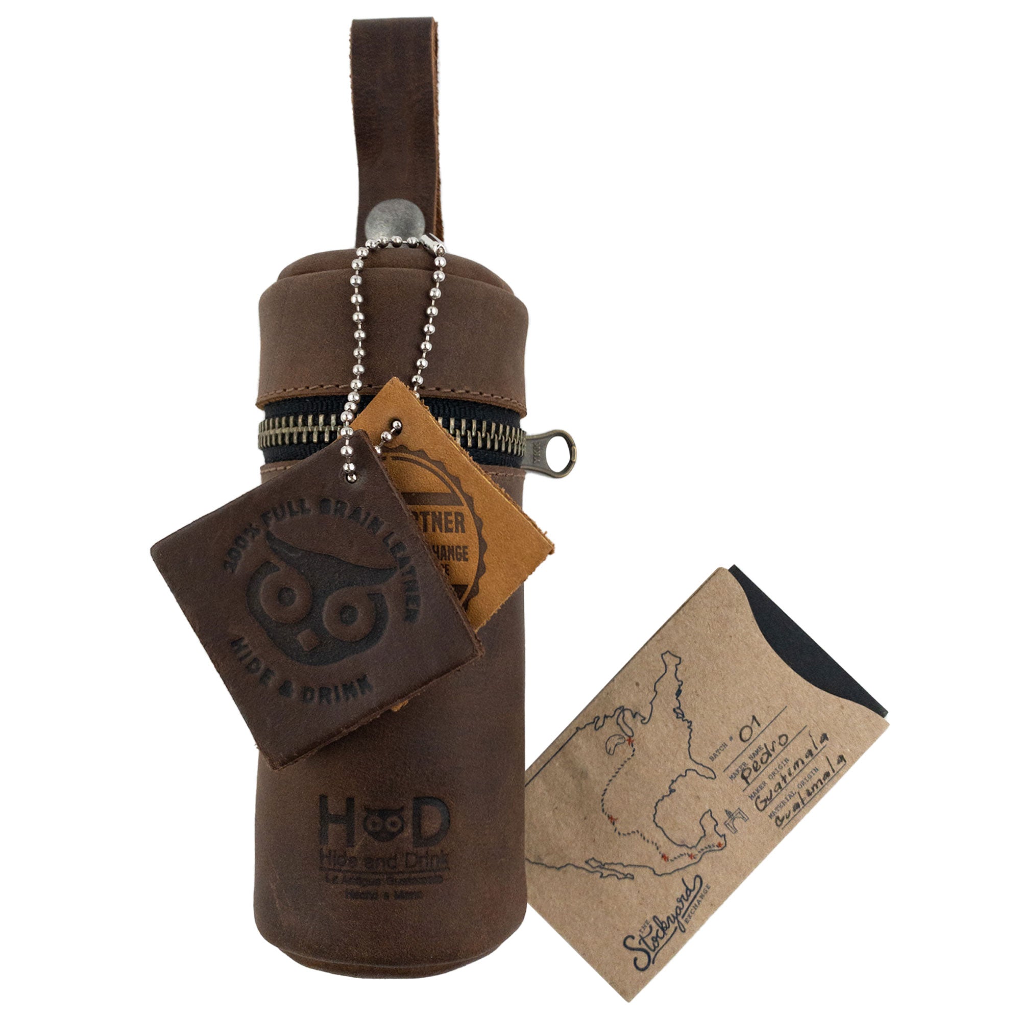 Hide & Drink Cylinder Case for Golf Balls presented alongside branding and packaging materials, showcasing the rustic elegance of full grain leather. This handmade accessory symbolizes the dedication to artisan craftsmanship and small batch production from La Antigua Guatemala & Oaxaca Mexico, making it a unique sports & outdoors accessory.