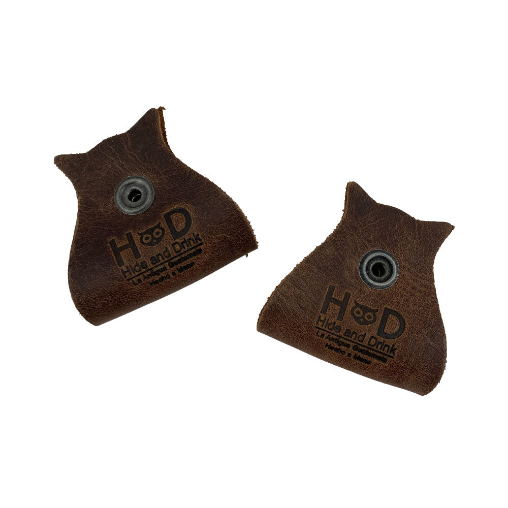 Charming Owl Shaped Cord Keeper (2-Pack) by Hide & Drink with the brand's logo featured prominently on high-quality brown leather keepers. Owl Shaped Cord Keeper (Cord Clam) 2-Pack. Full Grain Leather, StockyardX, Small Batch Production, Hand Cut, Hand Sewn, Fire Branded, Artisan, Handmade in La Antigua Guatemala & Oaxaca Mexico.